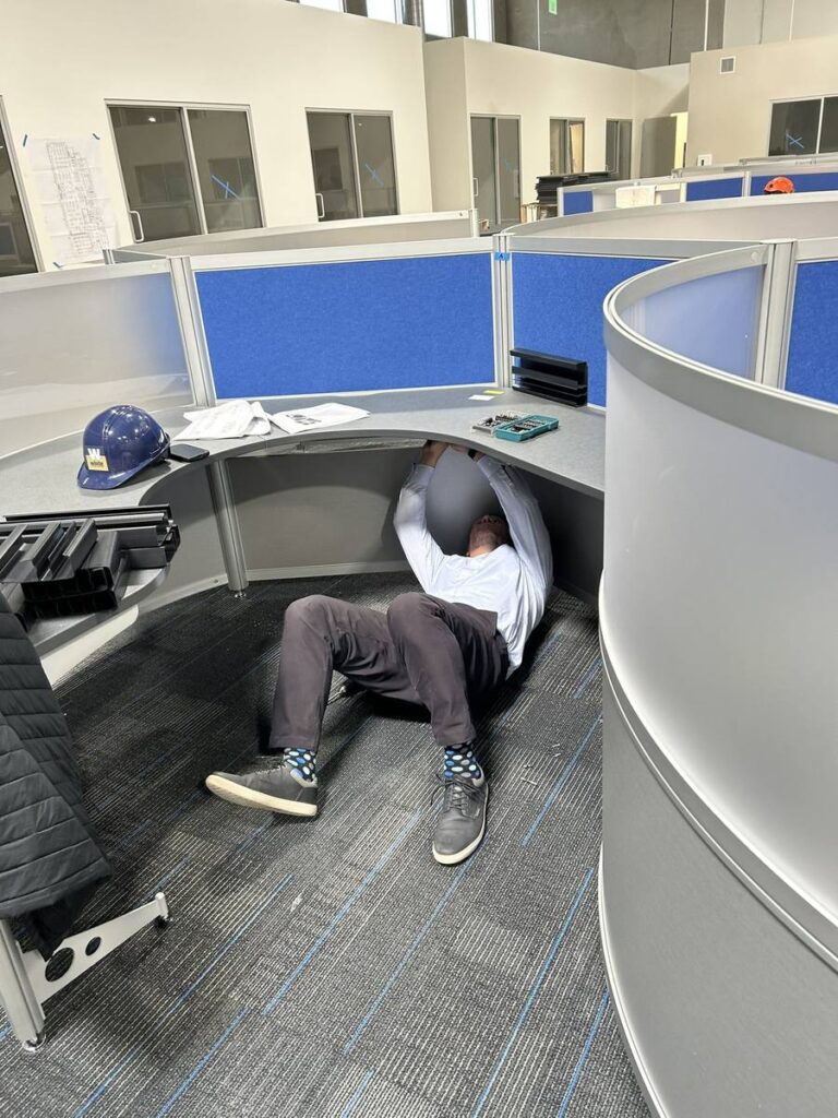Every inch matters: installer completing the final cable routing inside a contemporary curvilinear workstation, ensuring seamless wire management at every one of the 500 modern office cubicle stations.