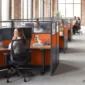 Modular cubicles with orange acoustic fabric panels, charcoal frame, clear acrylic toppers and walnut height-adjustable desks along a center corridor